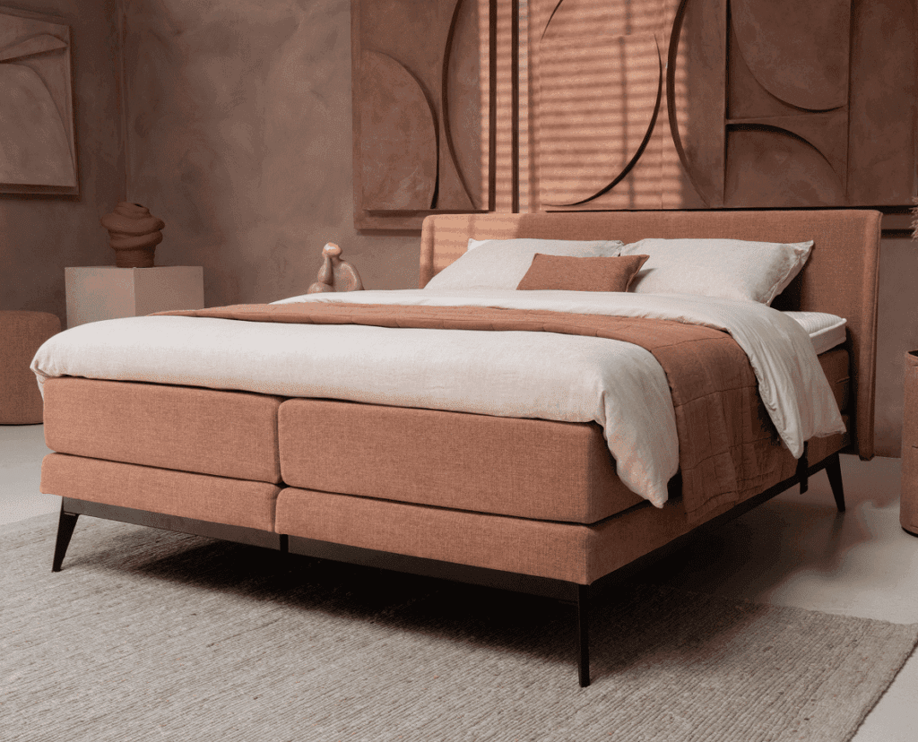 Boxspring in warme beige kleur met slanke zwarte poten in sfeervolle slaapkamer.