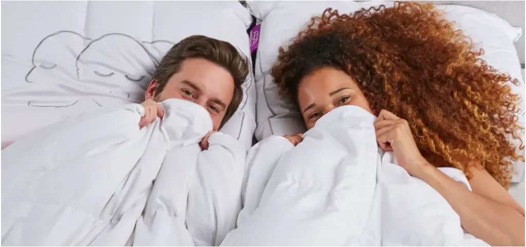 Stel ligt comfortabel in bed onder wit dekbed